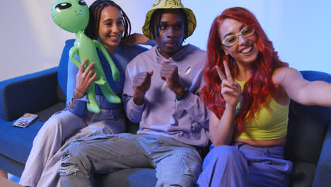 Studio-Shot-Of-Group-Of-Gen-Z-Friends-Sitting-On-Sofa-Posing-For-Selfie-With-Toy-Alien-On-Mobile-Phone